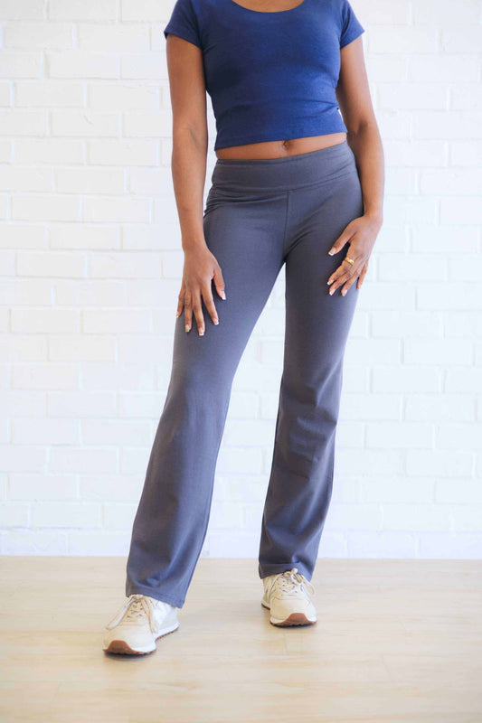 woman wearing gray hemp yoga pants and blue crop top standing against white wall