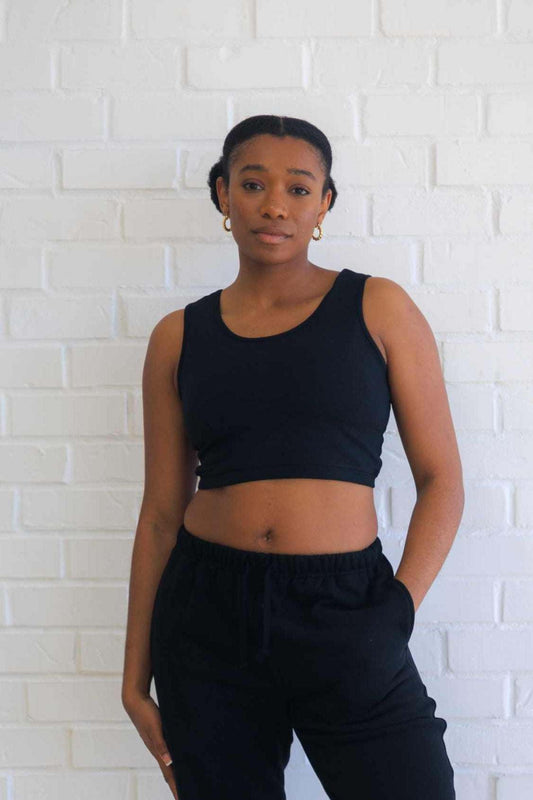 Woman wearing black hemp bralette and black pants standing against white brick wall