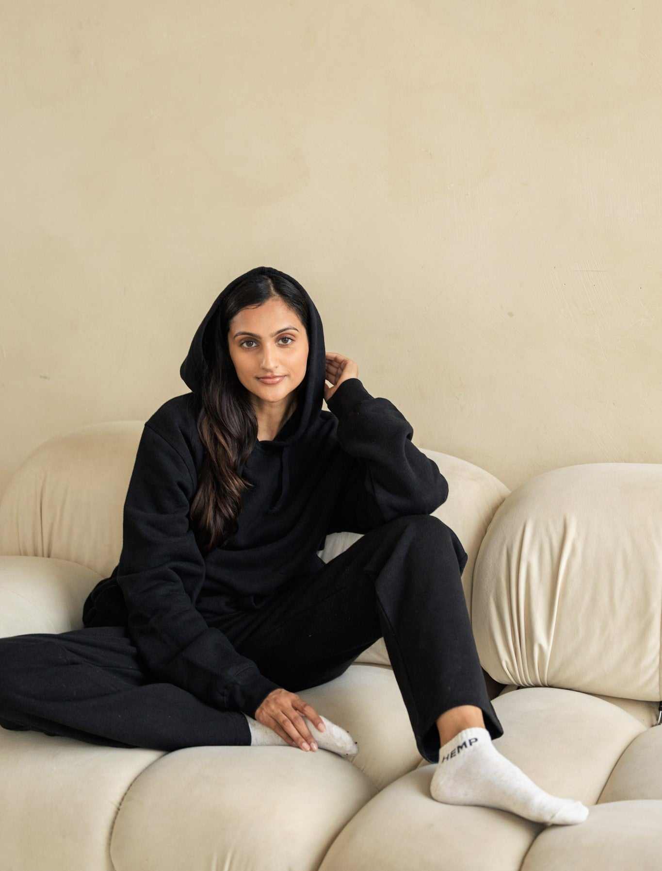Woman in black outfit sitting on a beige couch against a beige wall