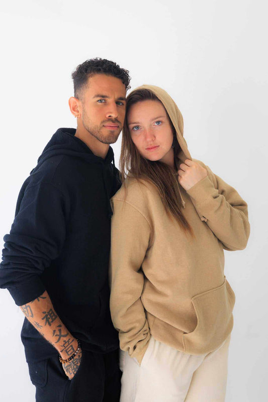 Two models wearing unisex hemp hoodies in black and taupe, styled casually with front kangaroo pockets and drawstring hoods.