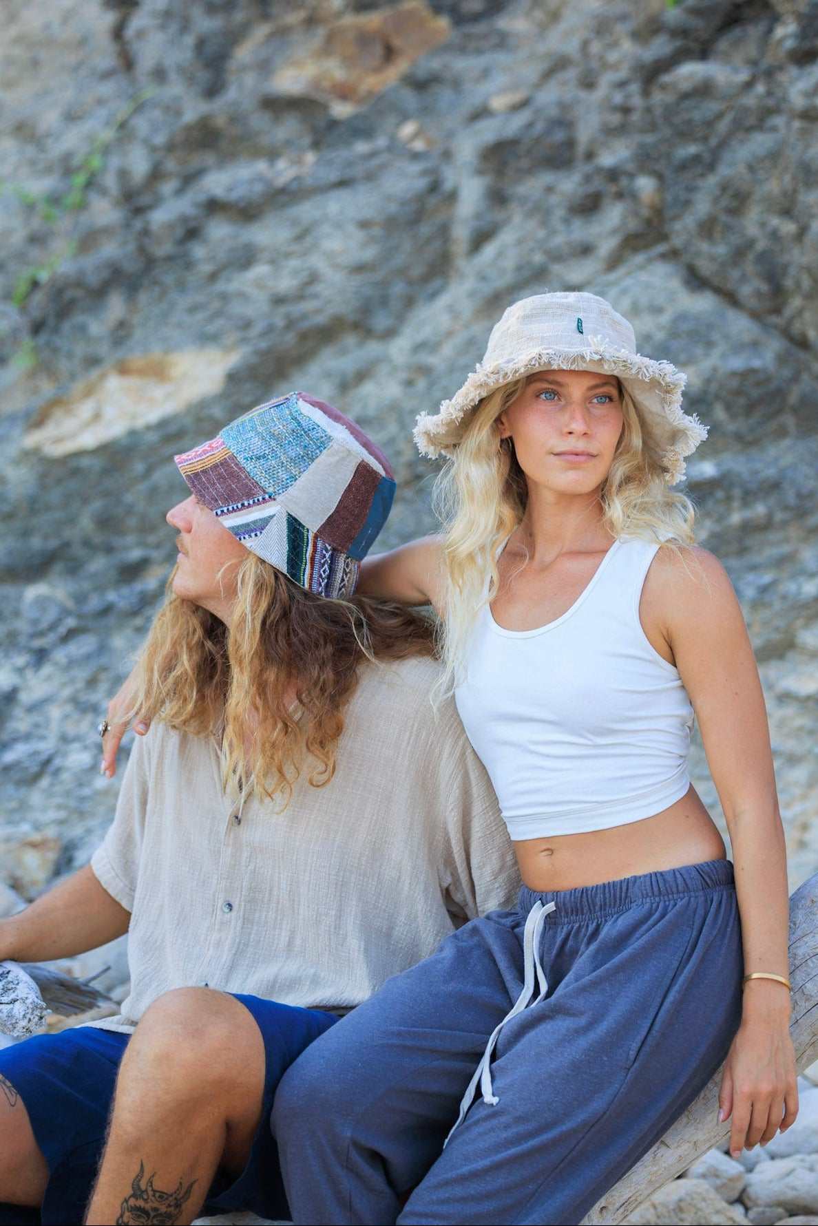 Two women sitting on a rocky beach with a textured stone wall background
