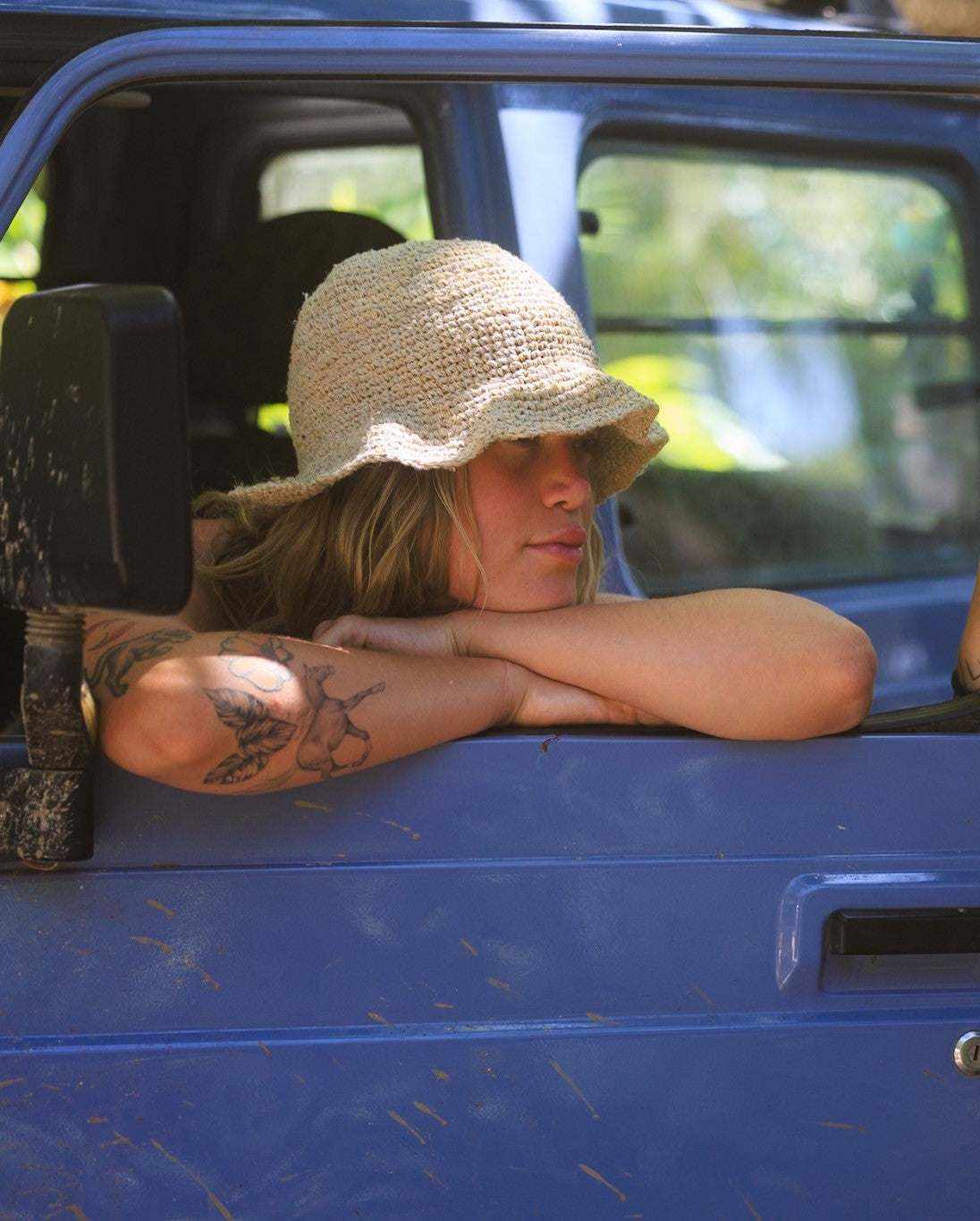 Hemp crochet floppy beach hat in natural color worn by a person sitting in a blue vehicle, showcasing boho style and foldable design.
