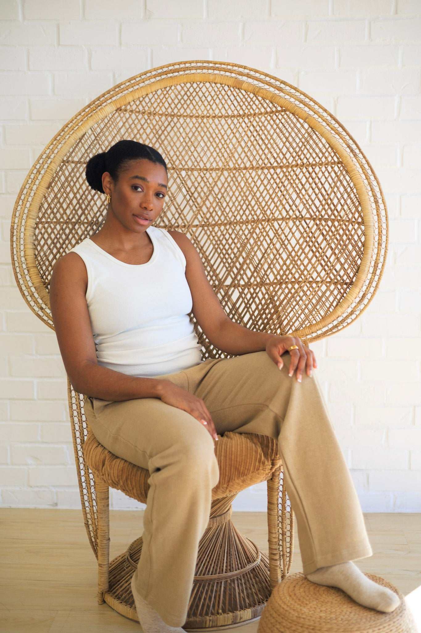 Woman sitting on a wicker chair against a white brick wall.
