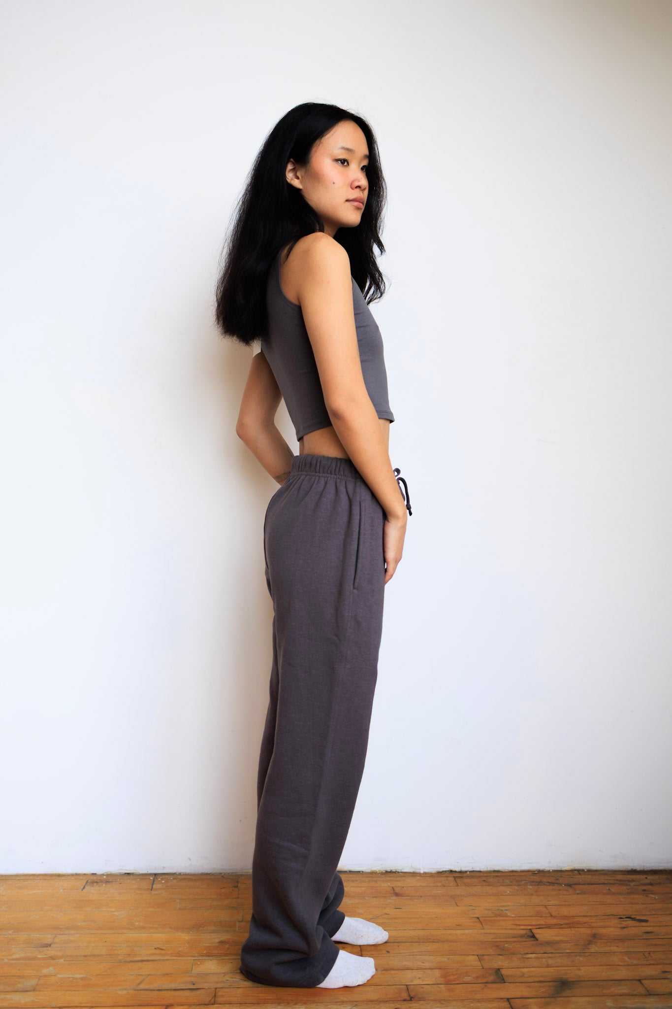 Woman wearing a gray sleeveless top and wide-leg pants against a white wall.