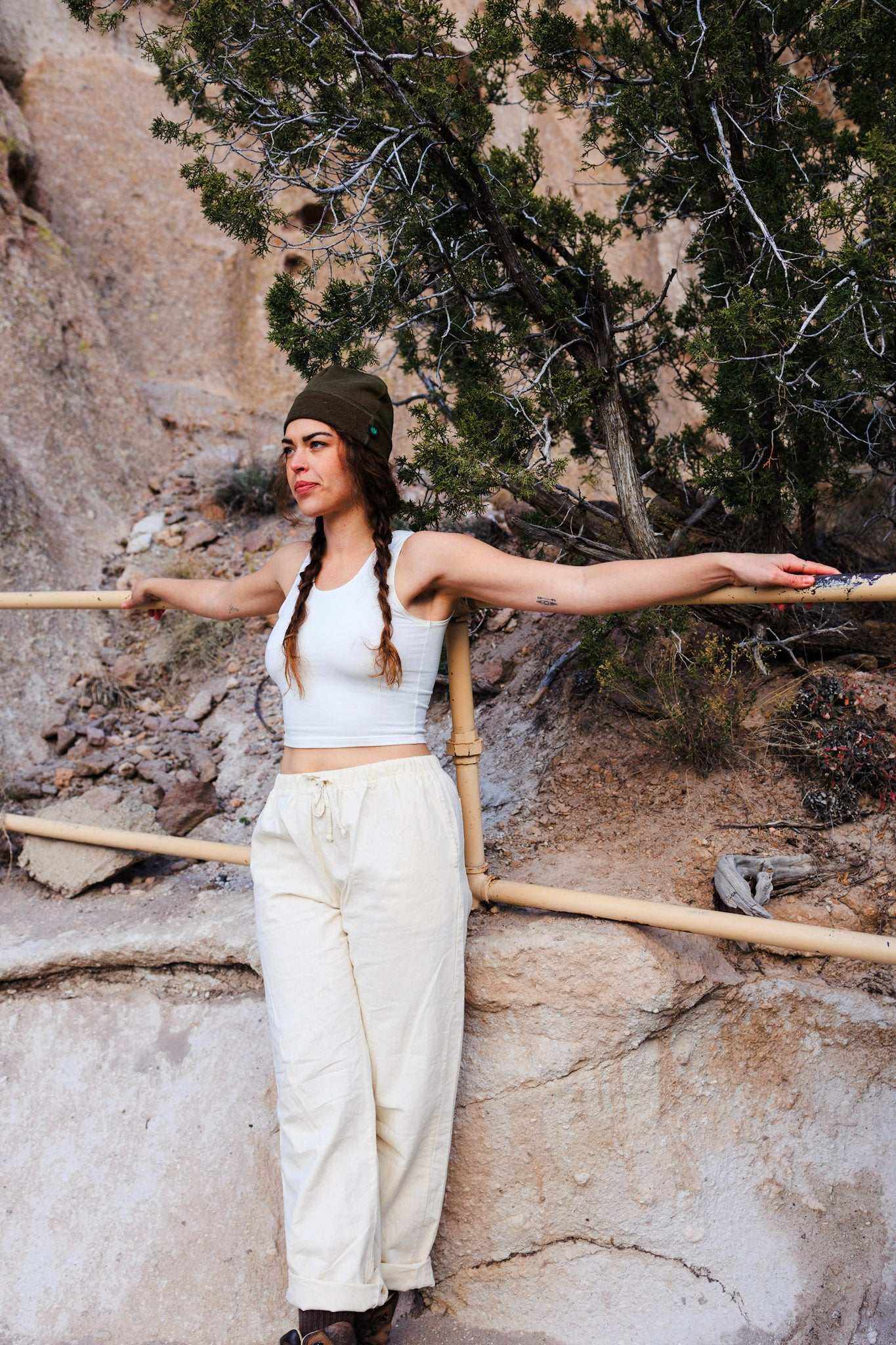 Woman in nature wearing unisex hemp linen and organic cotton pants, paired with a white crop top and olive beanie.