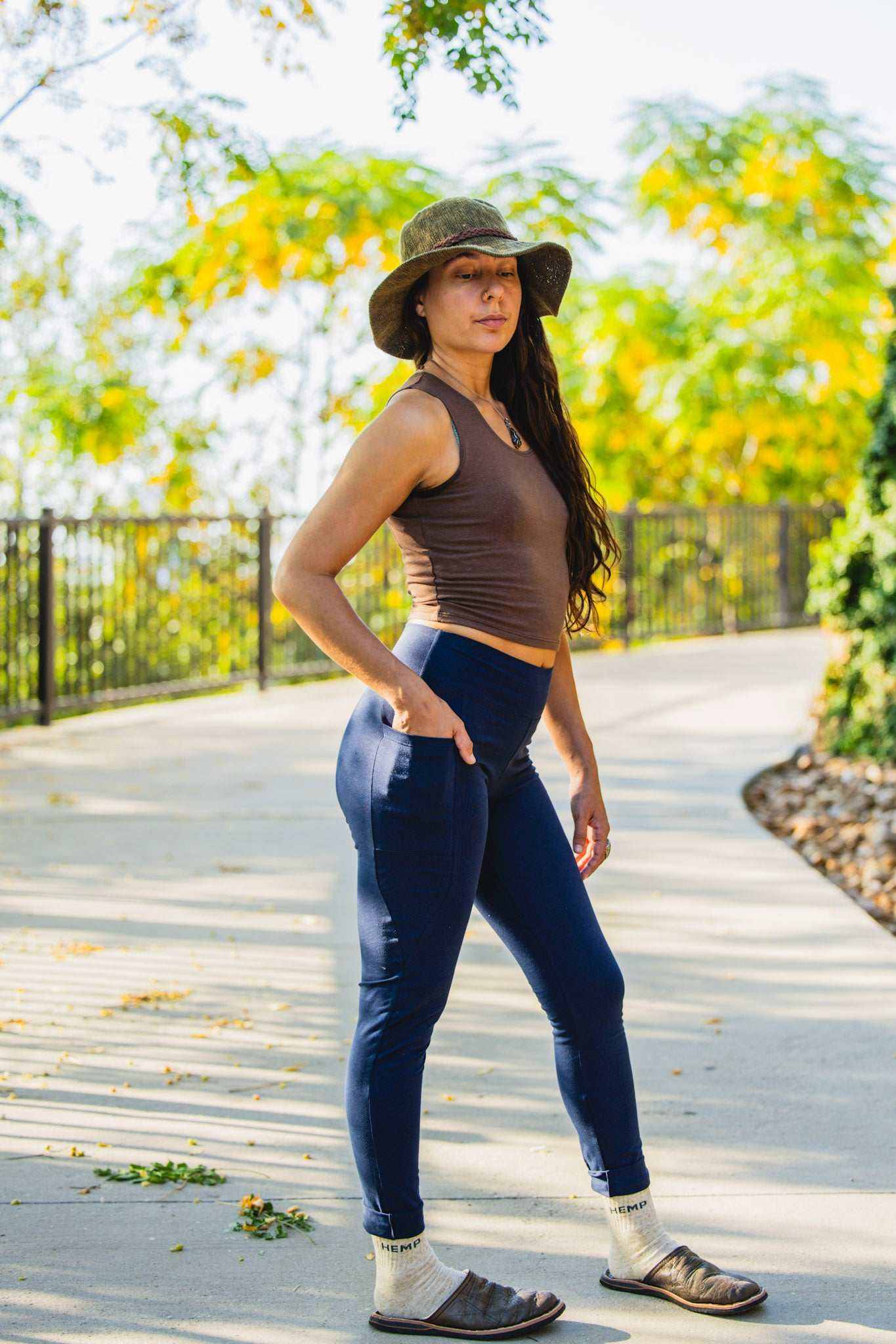 Woman wearing navy hemp leggings with side pockets and a brown sleeveless top outdoors on a sunny pathway