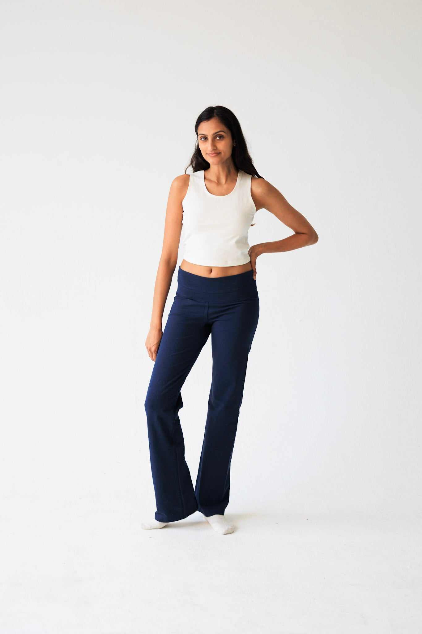 Woman wearing a white tank top and navy blue flared pants on a white background