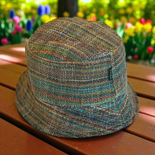 Multicolored woven bucket hat on a wooden surface with blurred floral background
