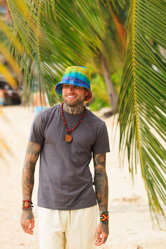 Man wearing a colorful bucket hat and gray t-shirt standing in front of palm trees.