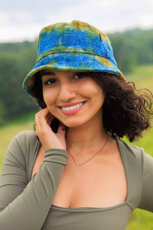 Tie dye bucket hat made from hemp in blue and green colors worn by a person outdoors.