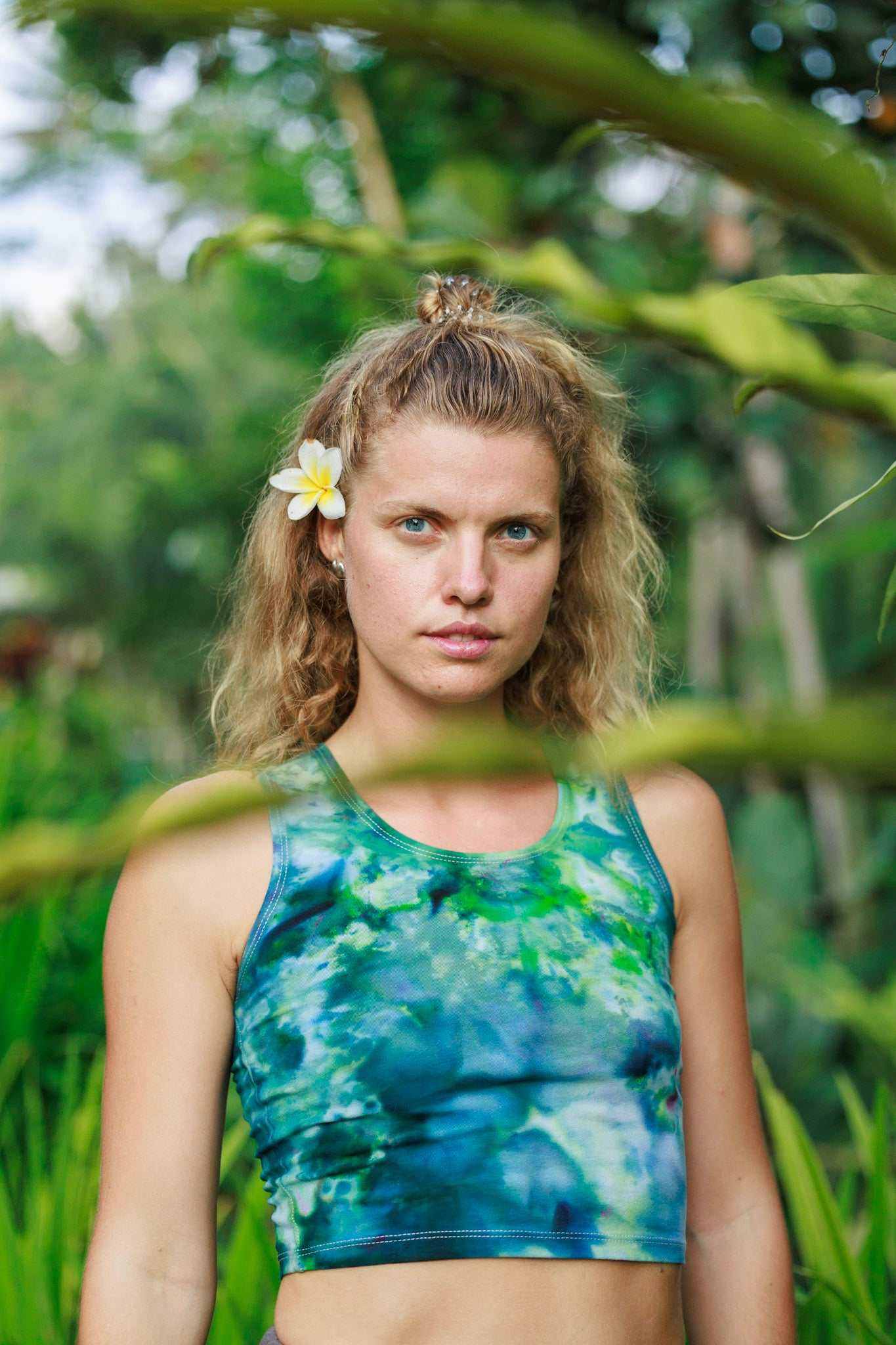 Hemp crop top tank in tie dye blue green worn by woman in lush outdoor setting.