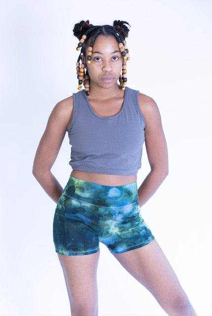Woman wearing blue and green tie dye hemp and cotton blend yoga shorts with pockets and a gray sleeveless crop top