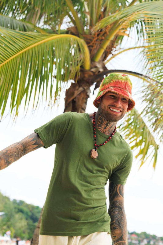 Man wearing colorful tie dye bucket hat and green t-shirt outdoors with palm tree background