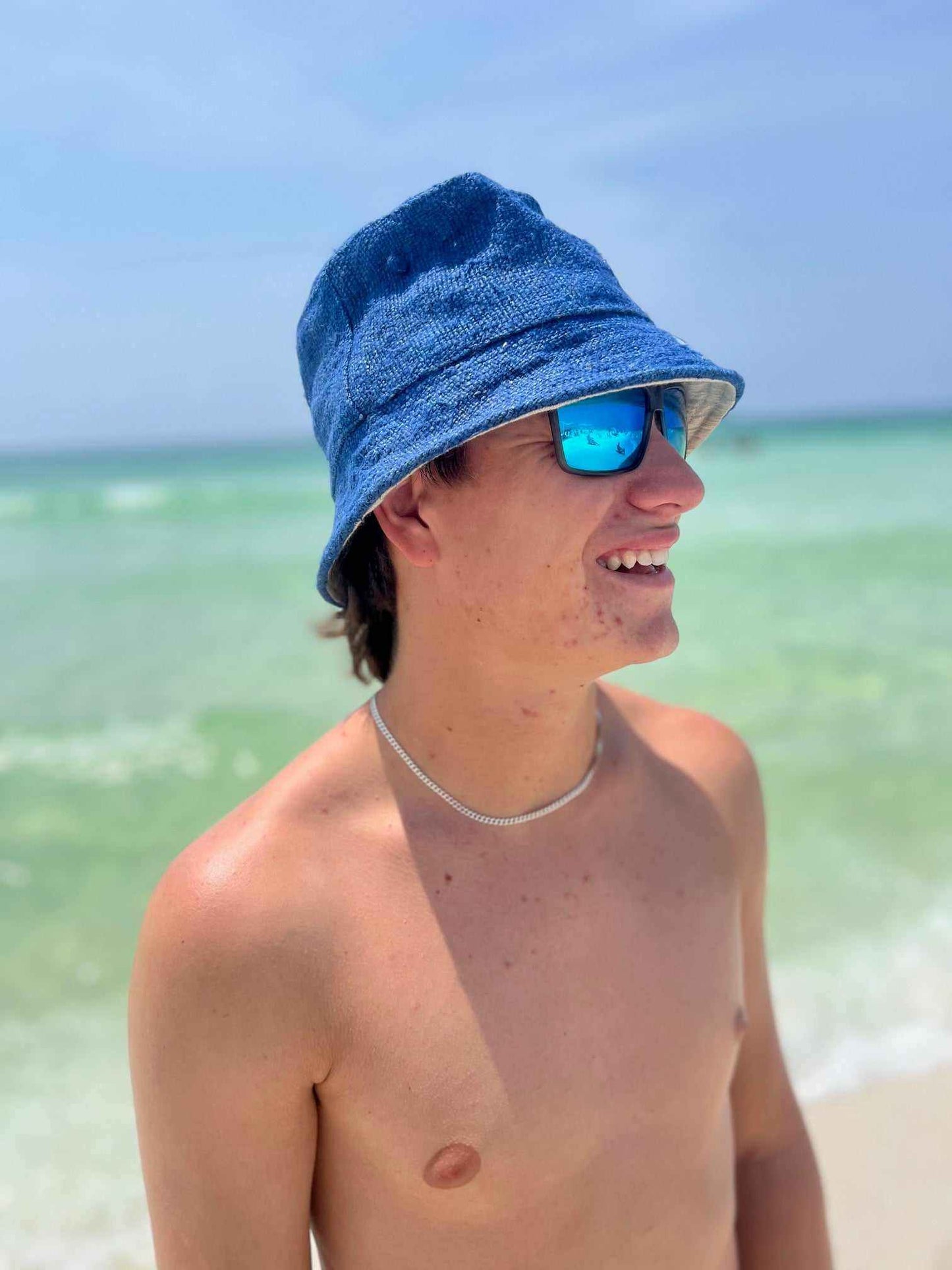 Man wearing blue hemp bucket hat on beach with ocean background.