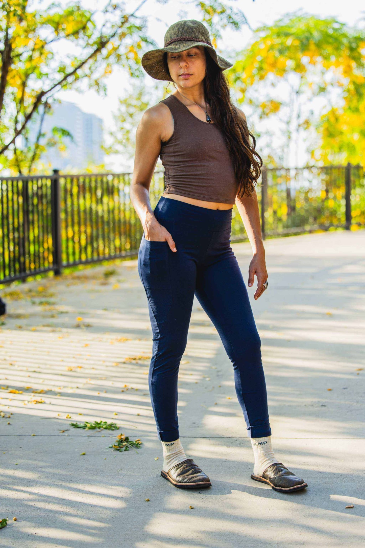 Woman wearing navy hemp leggings with pockets and a brown tank top outdoors on a sunny day