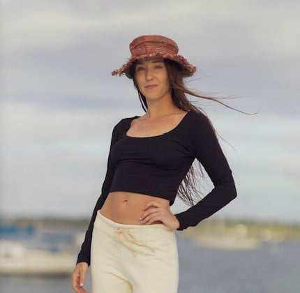 Woman wearing black hemp long sleeve yoga crop top with white pants and a brown hat outdoors