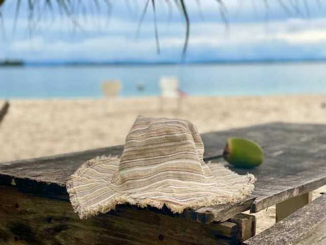 Hemp linen sun hat with wide brim resting on a wooden table at the beach.