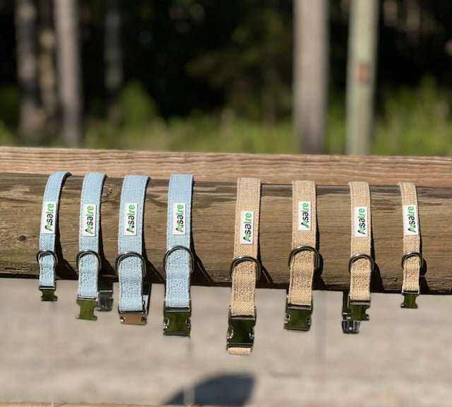 Hemp dog collars with metal buckles in denim blue and beige, displayed on a wooden railing.