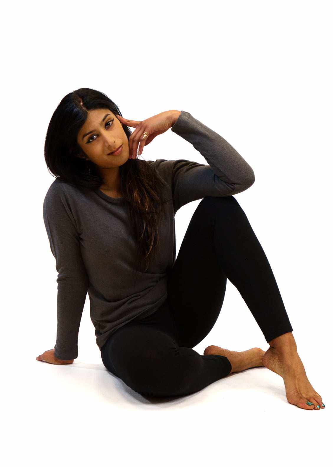 Woman wearing black hemp leggings with pockets and a long-sleeve gray top sitting on the floor