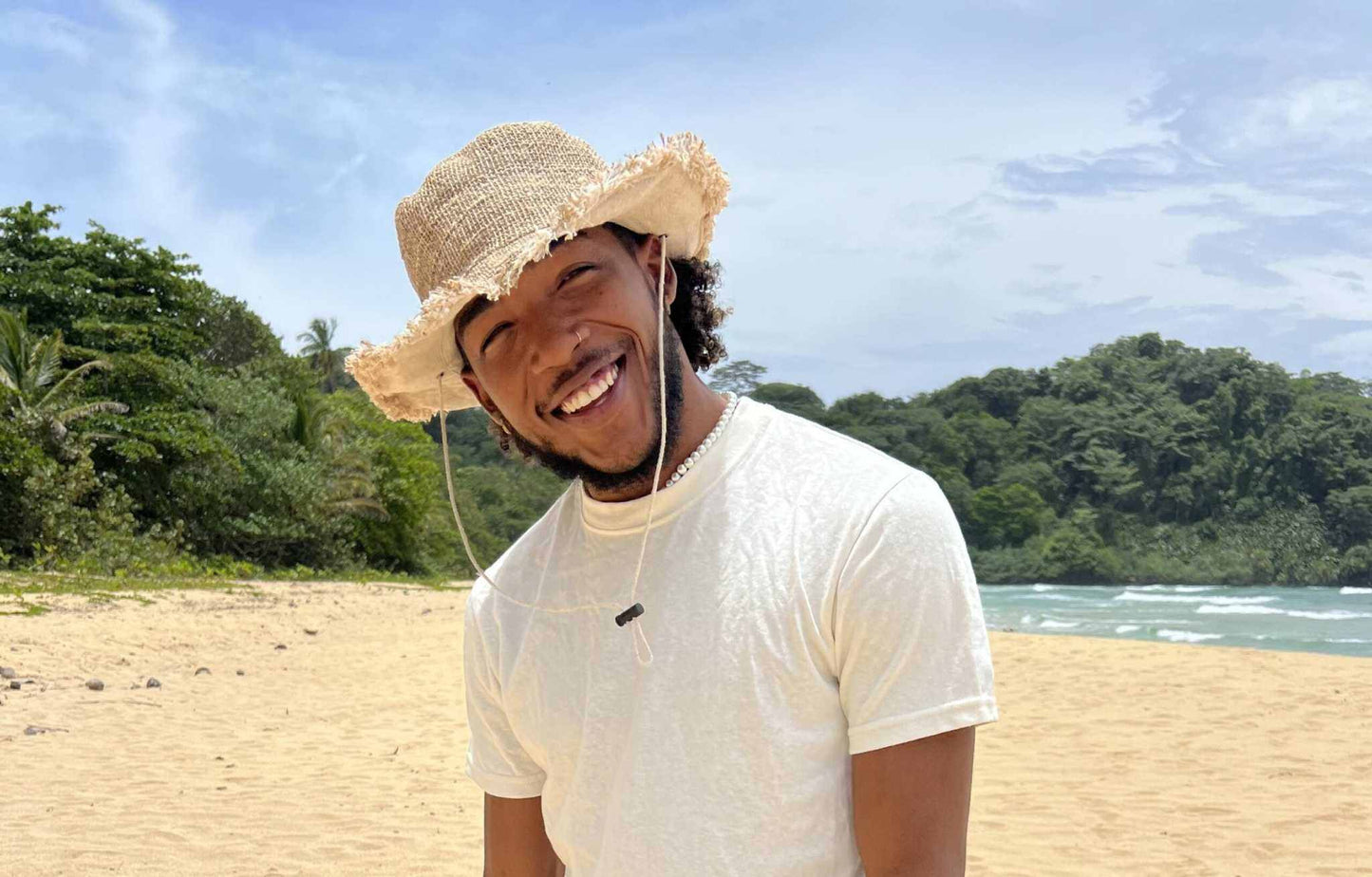Smiling person wearing a hemp safari hat with an adjustable chin strap on a sunny beach.