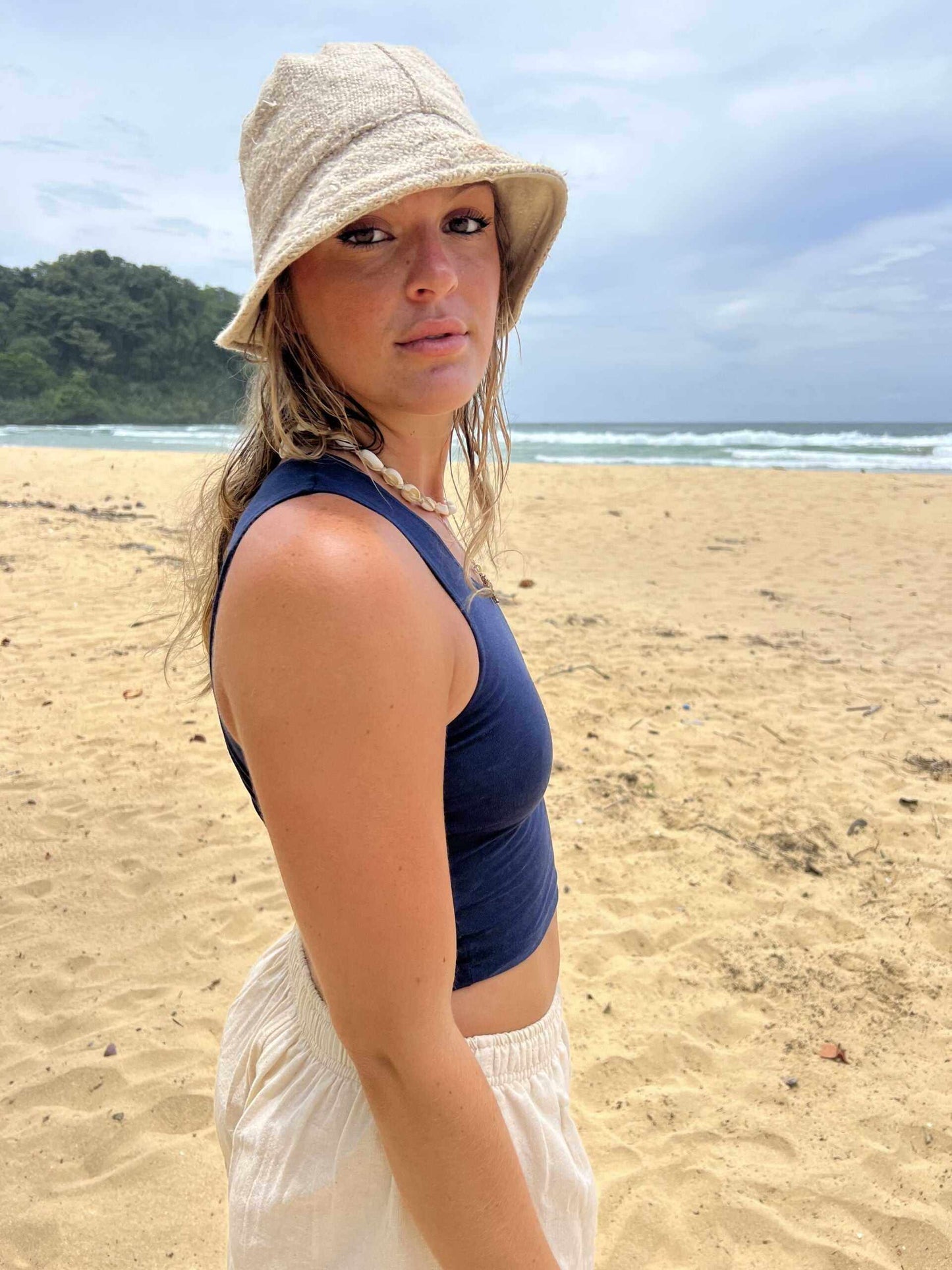 Eco-friendly hemp bucket hat in natural color, worn by a person on the beach.