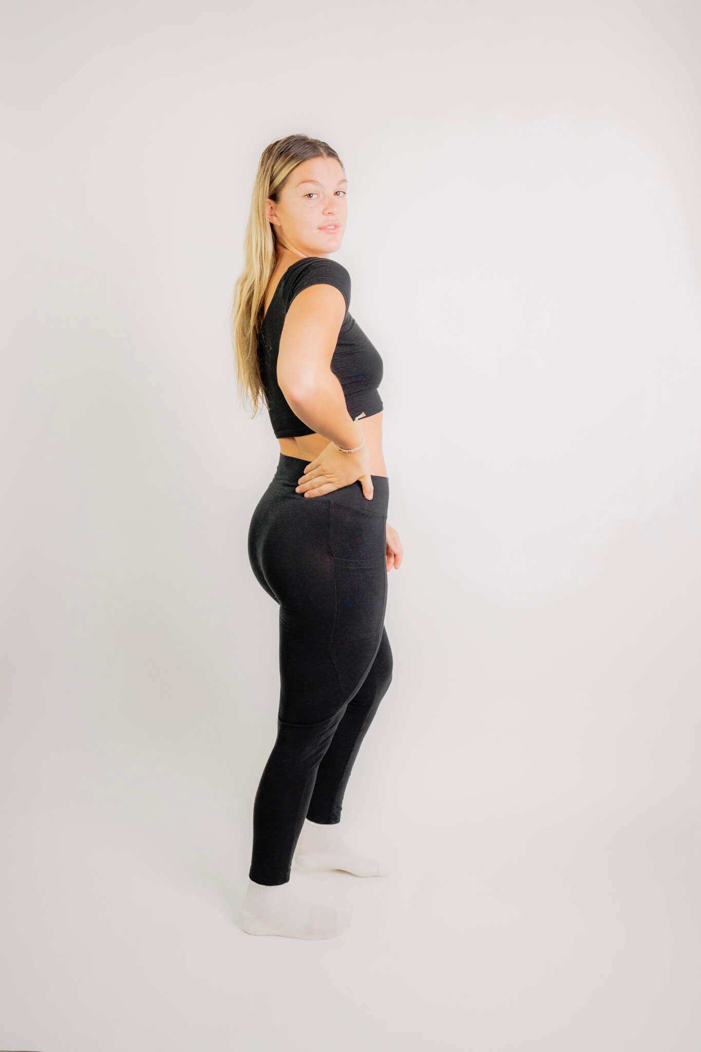 Woman wearing black sustainable hemp leggings with pockets, standing sideways against a plain background