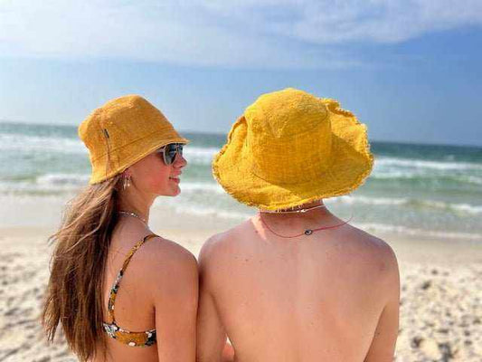 Golden hemp bucket hats worn by a couple on the beach with ocean waves in the background