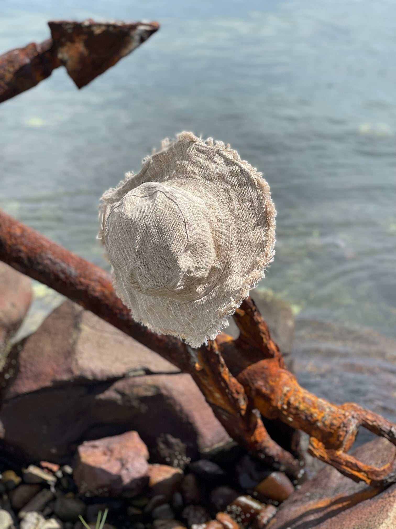 Hemp Linen Sun Hat in Neutral Stripe on a rusty anchor by the water.