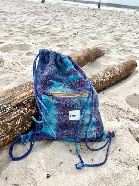 Tie dye hemp drawstring gym bag with front zipper pocket on sandy beach next to driftwood