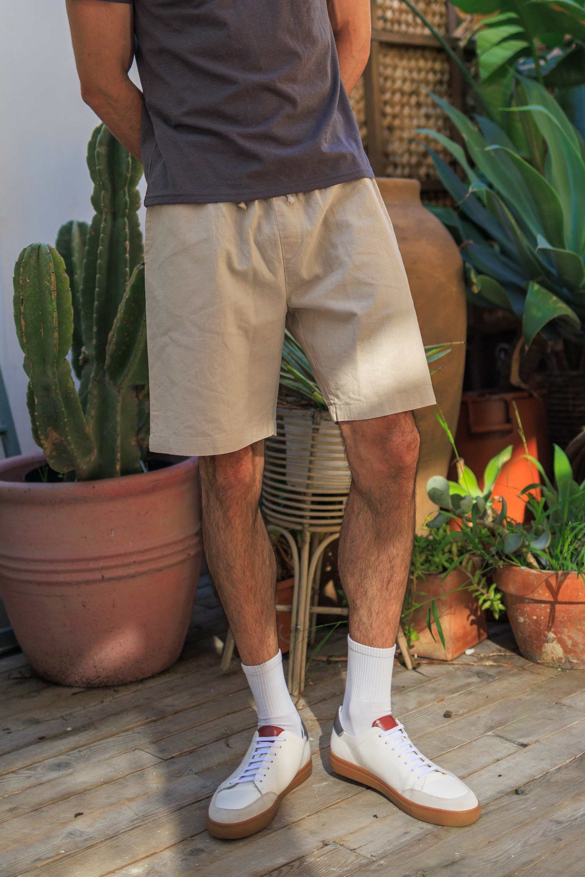Men's hemp linen shorts in beige with elastic waistband, styled casually outdoors with white sneakers.