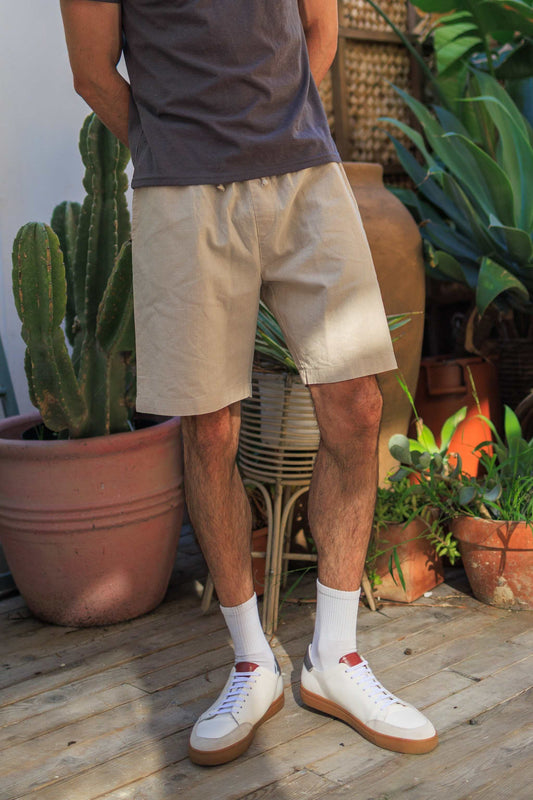 Men's hemp linen shorts in beige with elastic waistband, styled casually outdoors with white sneakers.