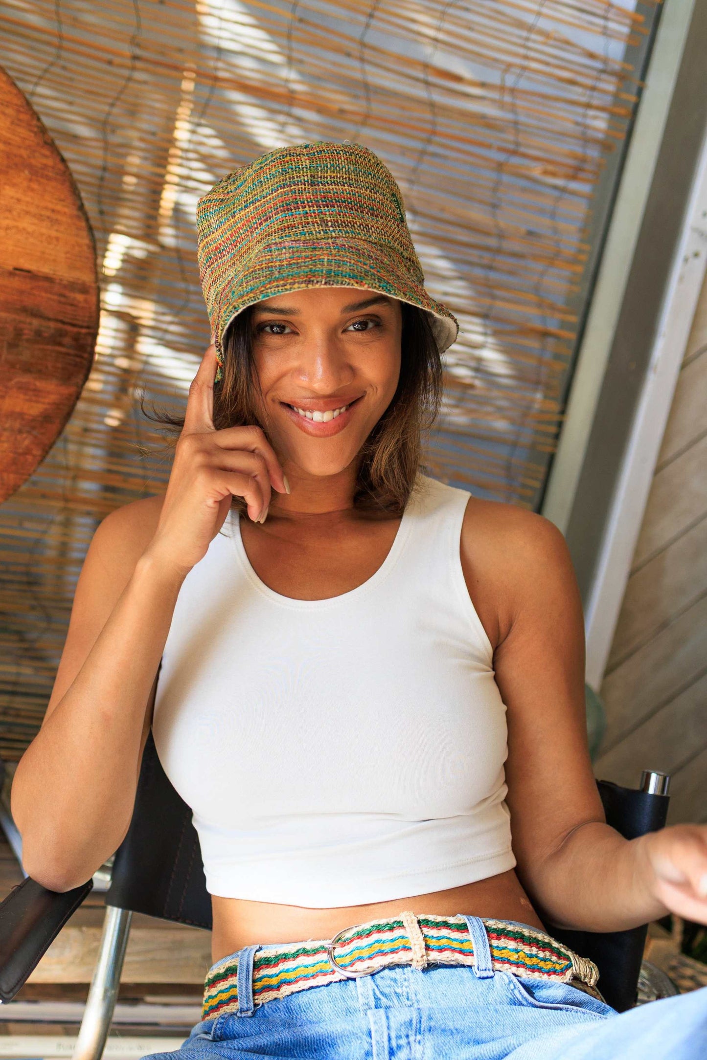 Woman wearing multi-color striped hemp bucket hat and casual white tank top sitting indoors