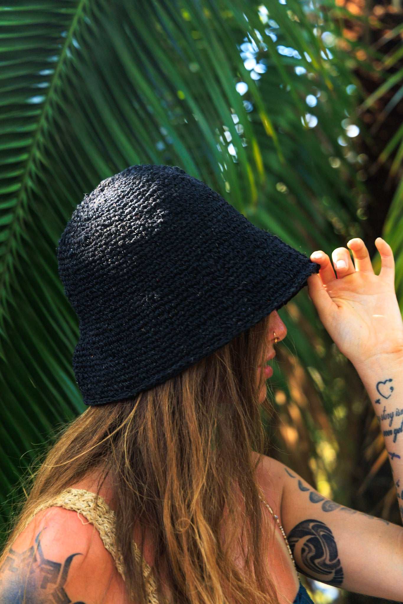 Person wearing a black woven hat with a tropical background