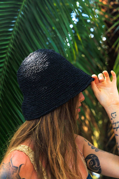 Person wearing a black woven hat with a tropical background