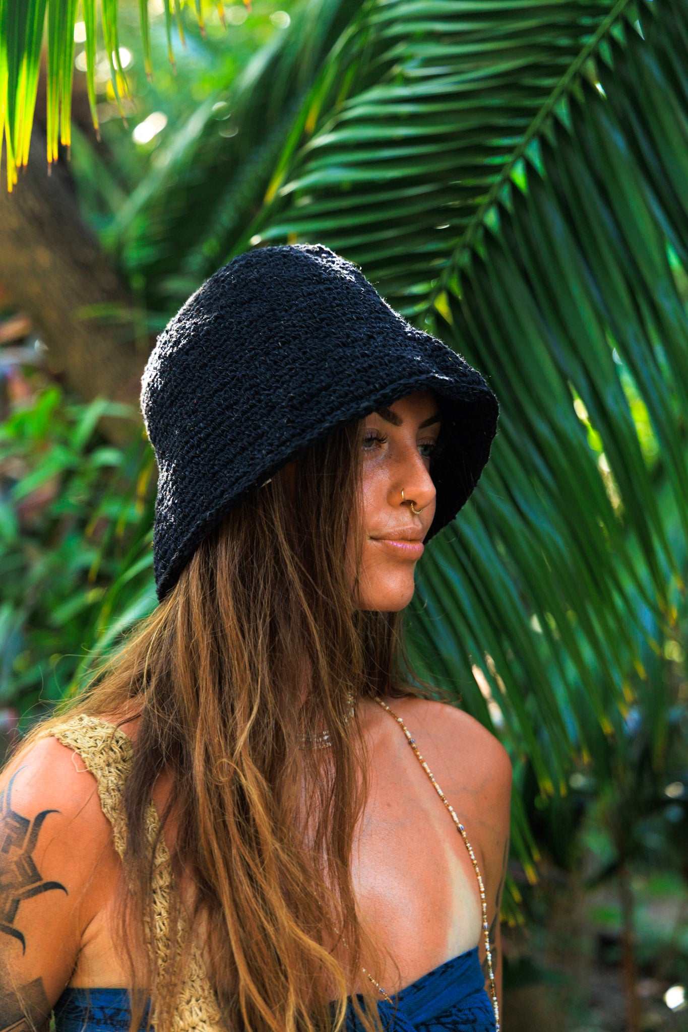Person wearing a black bucket hat in a tropical setting with palm leaves.