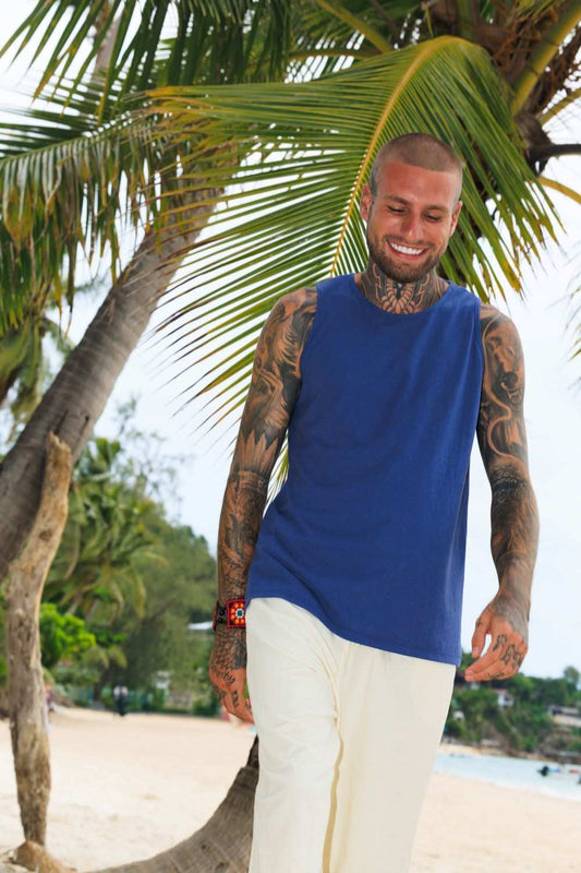 Man wearing blue men's hemp tank top walking on a tropical beach with palm trees