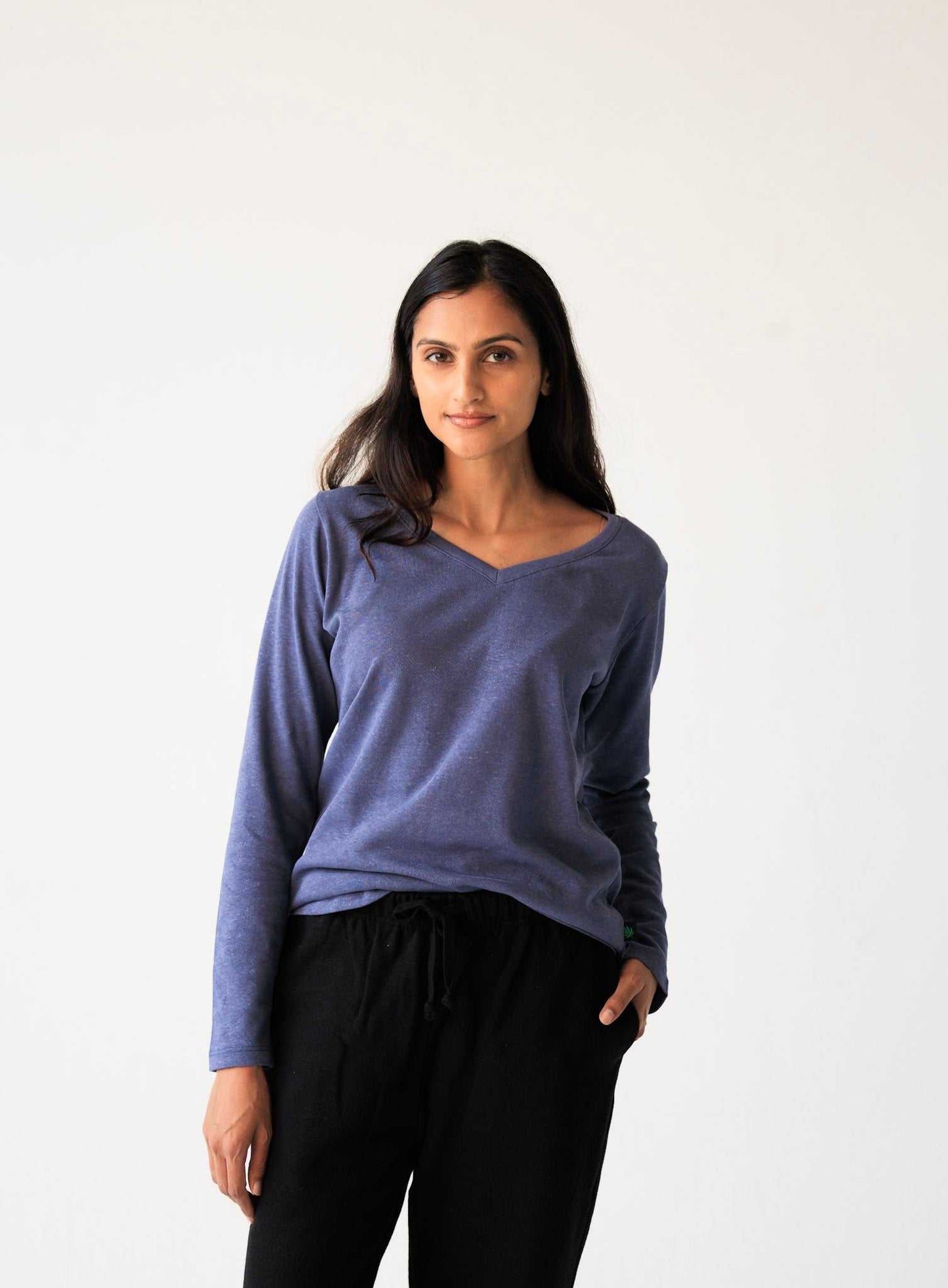 Woman wearing a blue long-sleeve top and black pants against a white background