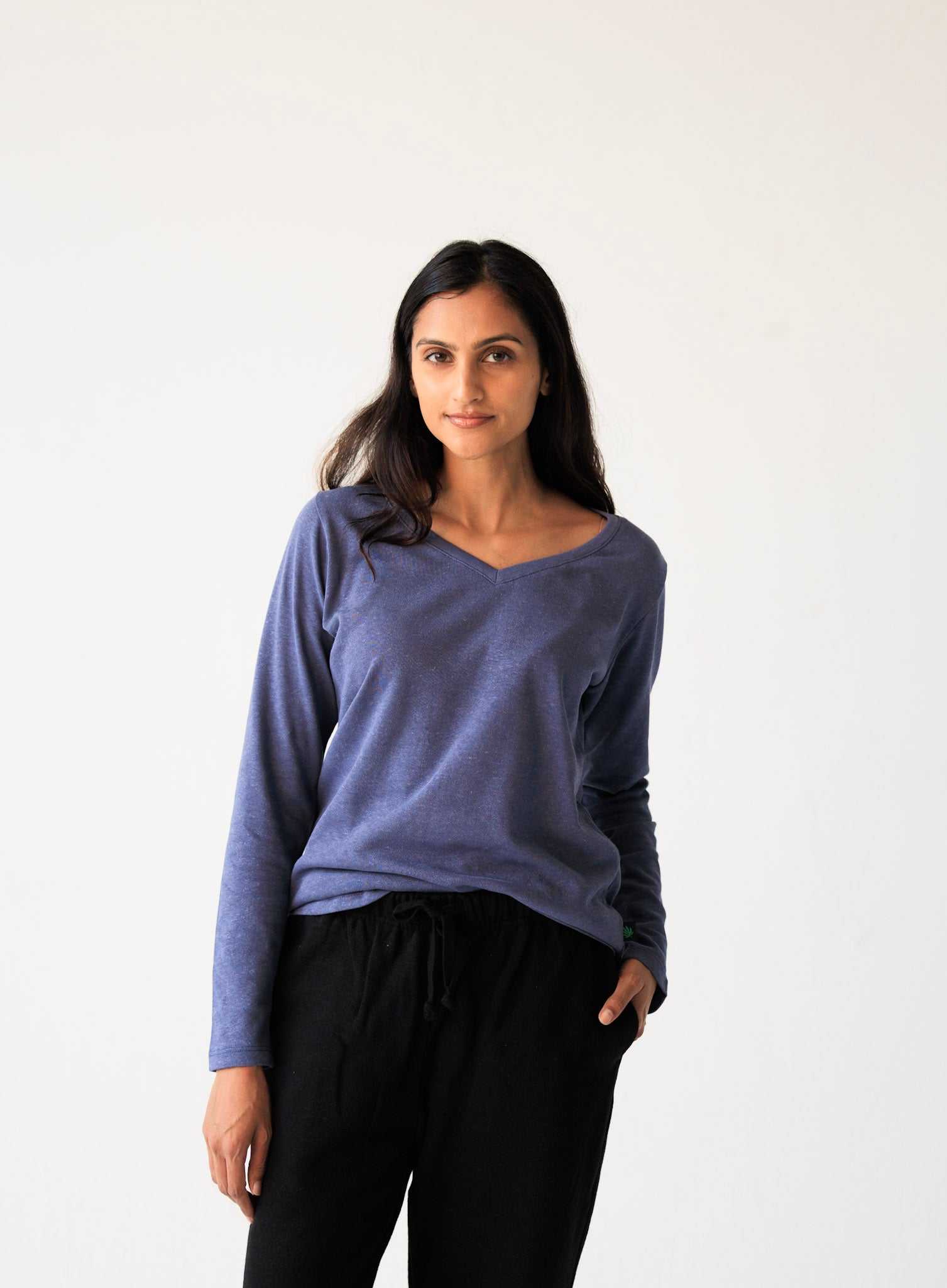 Woman wearing a blue long-sleeve top and black pants against a white background