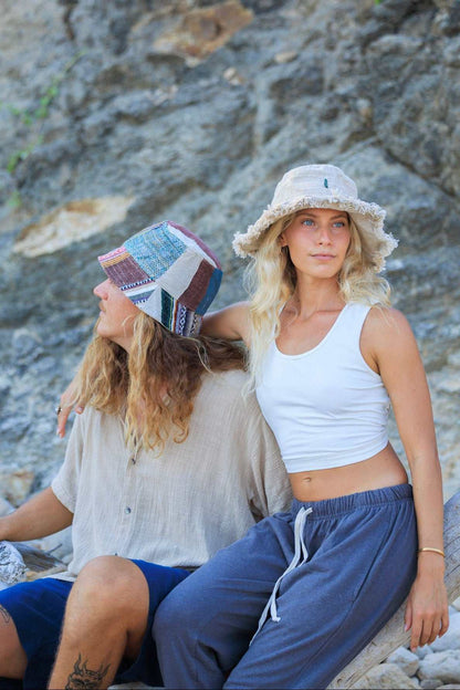 Two women sitting on a rocky beach with a textured stone wall background