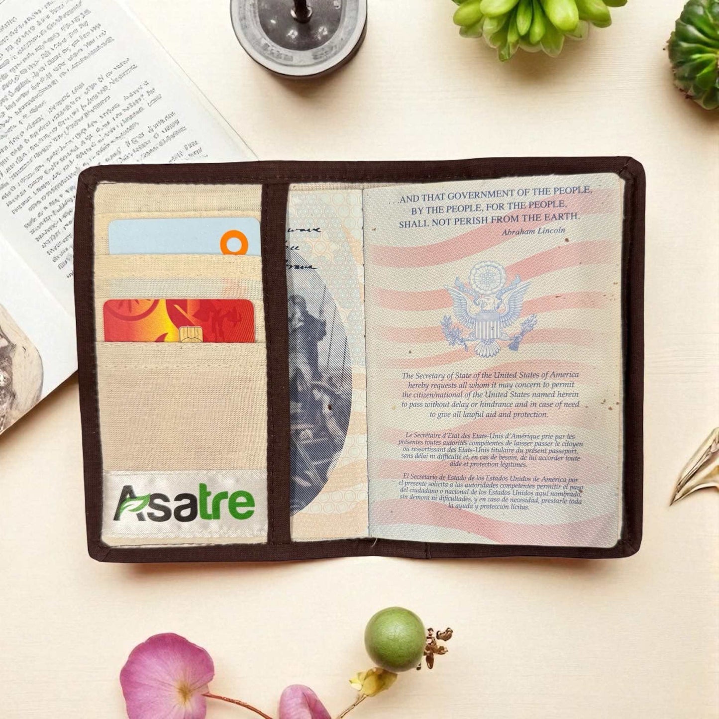Open passport holder with visible Asatre branding on a light surface with decorative elements.