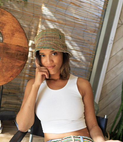 Woman wearing a patterned bucket hat and white top sitting outdoors.