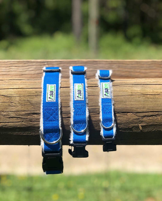 Three blue dog collars with a brand label on a wooden log outdoors.