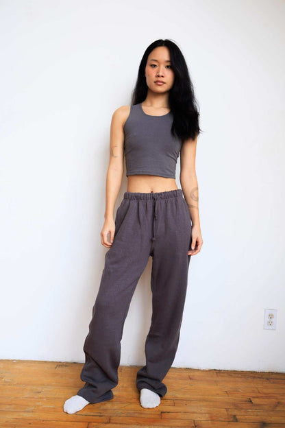 Woman wearing a gray tank top and wide-leg pants standing against a white wall.