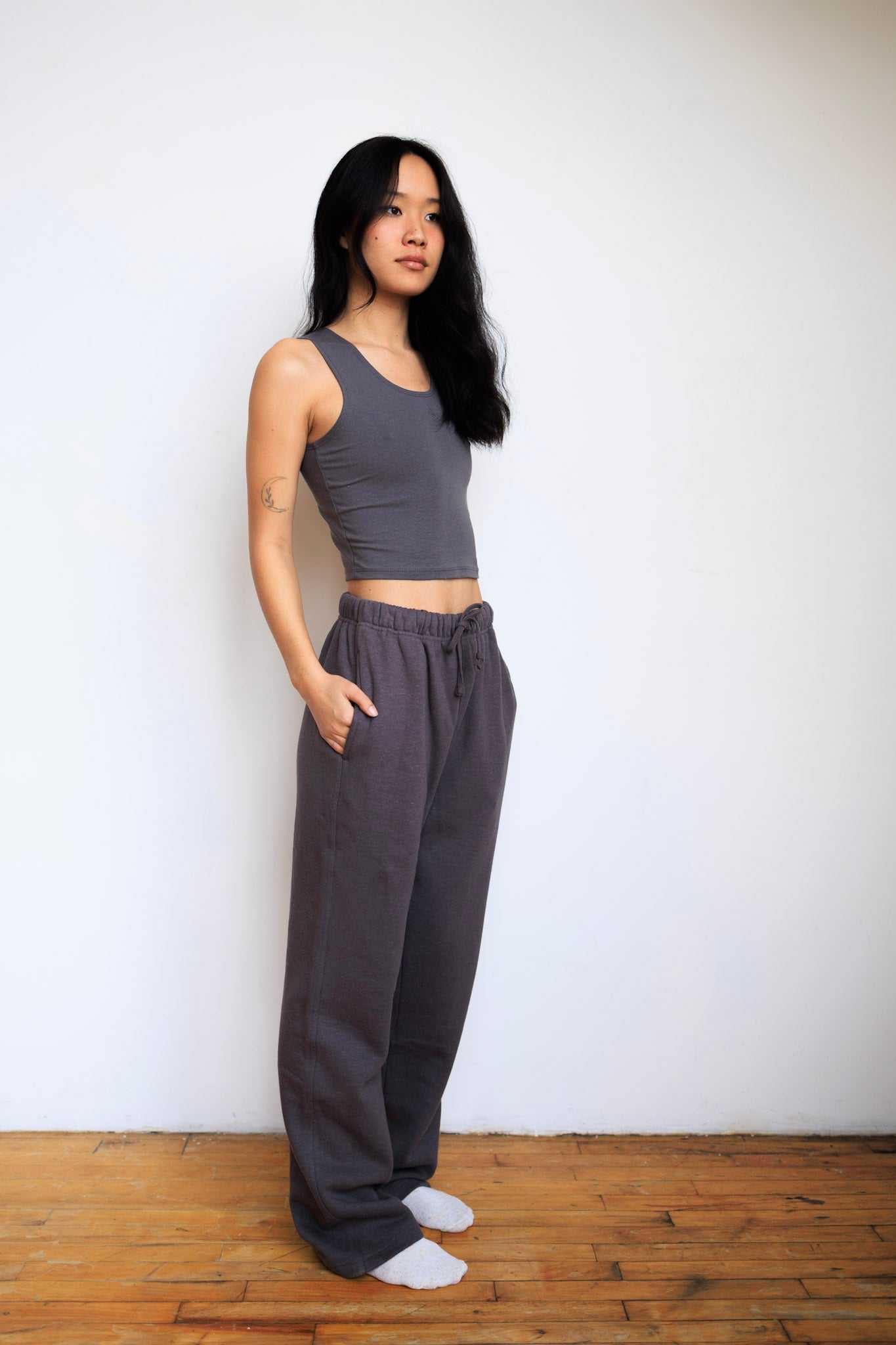 Woman wearing a gray tank top and wide-leg pants against a white wall.