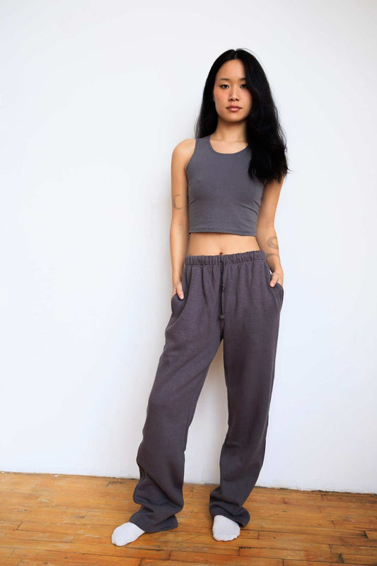 Woman wearing a gray tank top and wide-leg pants standing against a white wall.