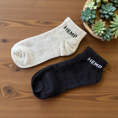 Pair of eco-friendly hemp ankle socks in natural and black colors on wooden surface with succulents nearby