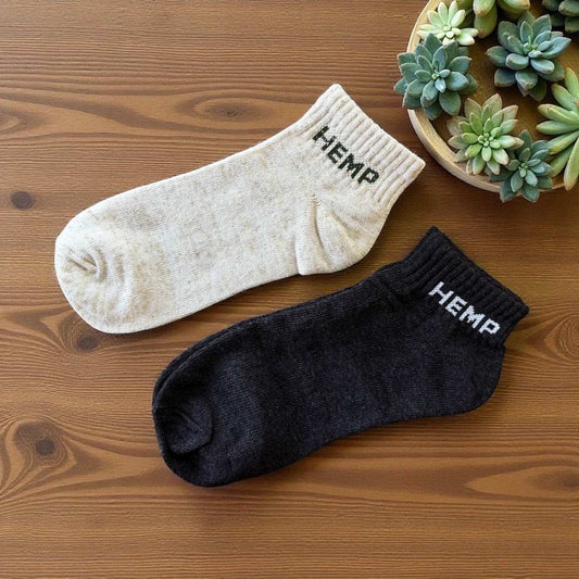 Pair of eco-friendly hemp ankle socks in natural and black colors on wooden surface with succulents nearby