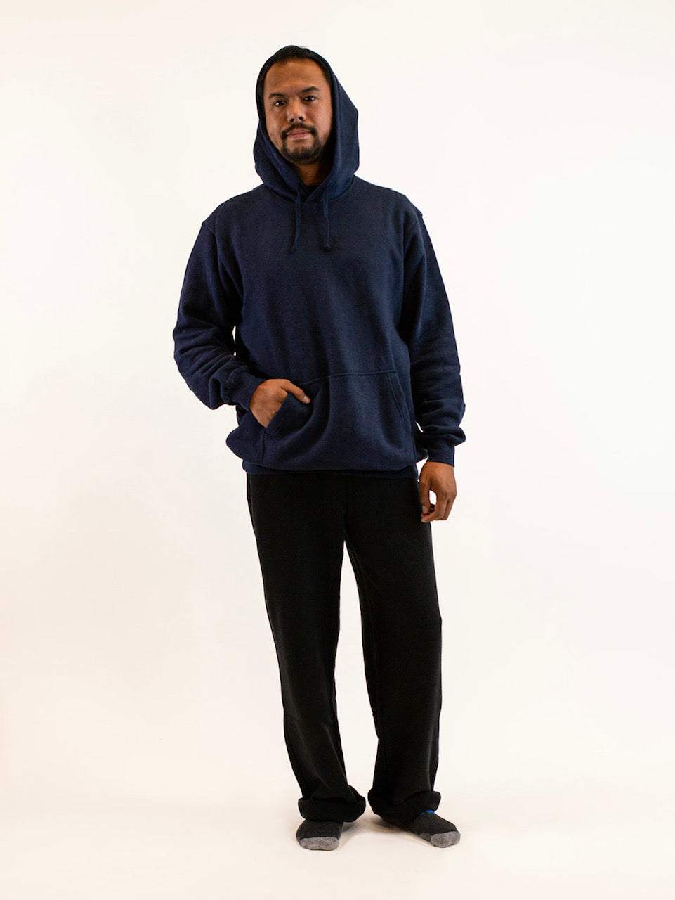 Person wearing a navy blue hoodie and black pants on a white background