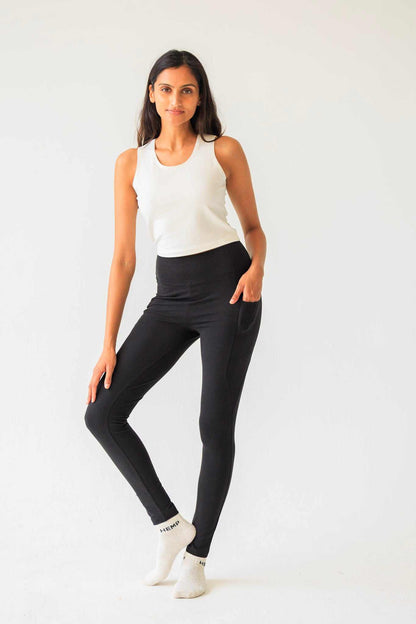 Woman wearing a white tank top and black leggings on a white background