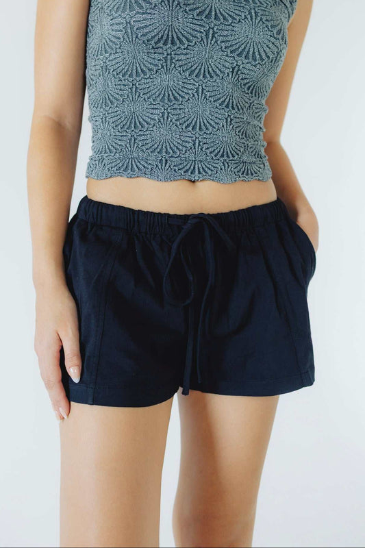 A model wearing a slate blue-gray textured crochet crop top and dark navy blue drawstring shorts against a plain white background.